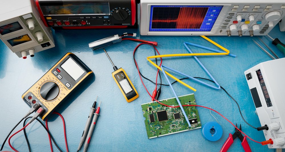 Electronics workbench with testing equipment connected to a circuit board; blue surface.